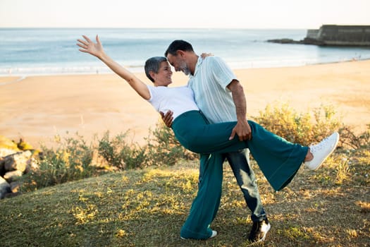 Senior couple swirling in dance at shore with ocean view
