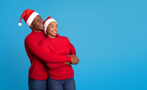 Black Couple In Festive Christmas Hats Embrace Against Blue Background