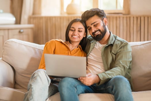 Young indian couple relaxing on couch, browsing together on laptop
