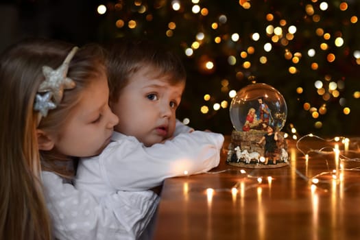 Brother and sister looking at a glass ball with a scene of the birth of Jesus Christ