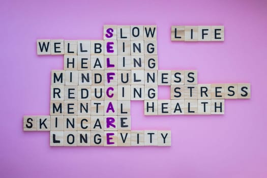 Top view of SELFCARE word on pink background. Minimalism creative crossword puzzle concept. Message of text Slow life wellbeing healing mindfulness reducing stress mental health skincare longevity