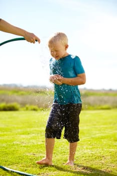 Kid, boy and hose pipe with splash, water fun and playing outdoor in backyard or garden for sunshine. Child, male and person on grass or lawn with happiness, activity and enjoyment in summer weather