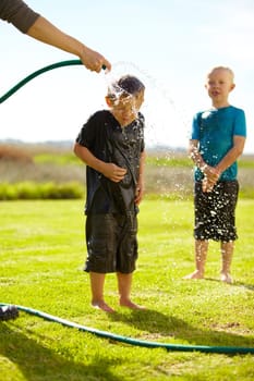 Children, boys and hose pipe with splash, water fun and playing outdoor in backyard or garden for sunshine. Kids, brother and people on grass or lawn with happiness, activity and enjoyment in summer