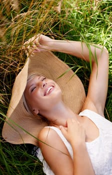 Grass, hat and woman relax on lawn with peace, happiness and freedom in summer. Outdoor, fashion and girl lying in field with smile on face for holiday, vacation or free time in nature with wellness