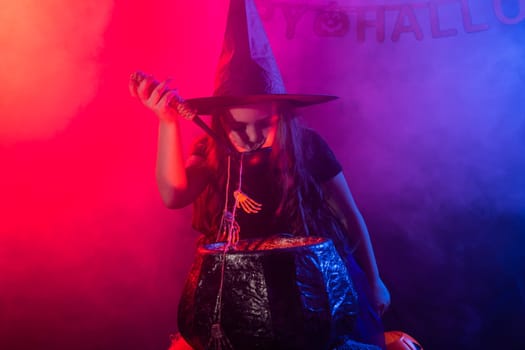 Little witch child cooking potion in the cauldron on Halloween.