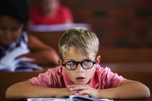 Classroom, student and boy with thinking, bored and education with glasses, learning and teaching. Kid, school and child with eyewear, development, notebook or tired with a test, morning and studying