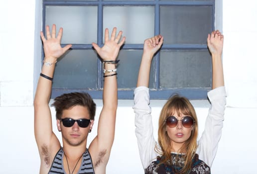 Couple, fashion and arms up with sunglasses, serious and wall for outdoor, urban and trendy. Clothes, teen and friendship with man, woman and youth as hipster, edgy and cool for funky, young or city