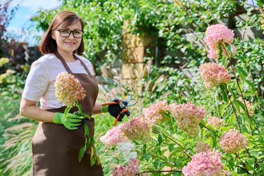 Portrait of gardener woman with pruner looking at camera in garden