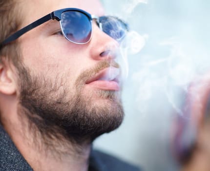 Face, man and smoking with sunglasses for experience, fun and cigarette enjoyment outdoor. Person, hipster and guy with smoke for exhale, serious and smoker with tobacco satisfaction and shades