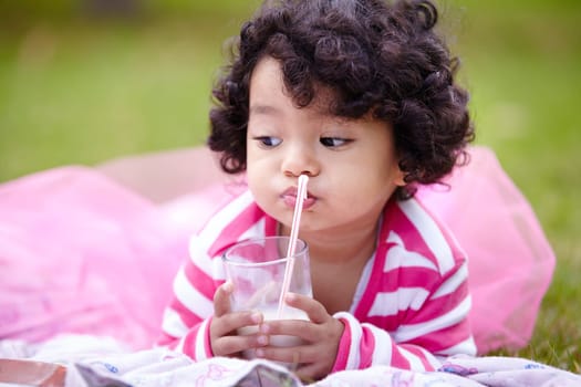 Girl, child and drinking of milk on grass with straw in pink tutu while lying for picnic. Youth, curly hair and kid with dairy for balanced diet, nutrition and calcium for development of strong bones