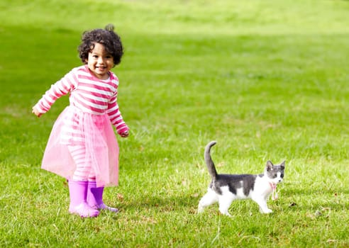 Nature, kitten and girl playing in a garden on the grass on a summer weekend together. Happy, sunshine and portrait of child walking and having fun with cat or feline animal pet on lawn in a field.