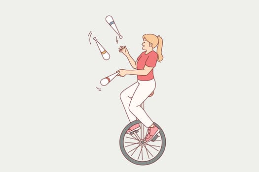 Agile woman rides unicycle and juggles pins, demonstrating tricks for audience of circus show