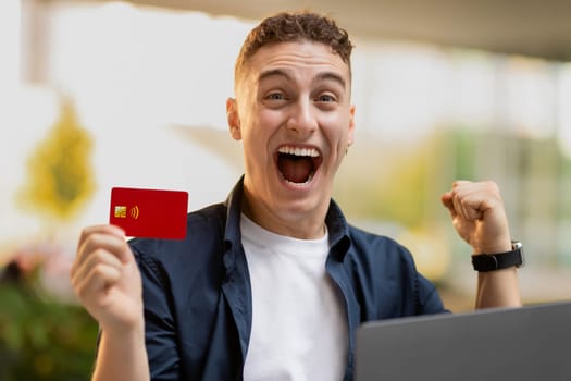 Happy excited millennial caucasian guy with open mouth, show credit card celebrate win