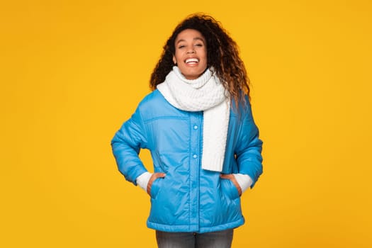 Cheerful black lady in winter attire posing over vibrant yellow background