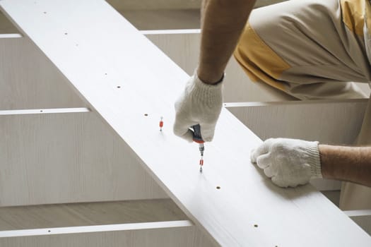 A male worker tightens fasteners on parts of cabinet furniture.