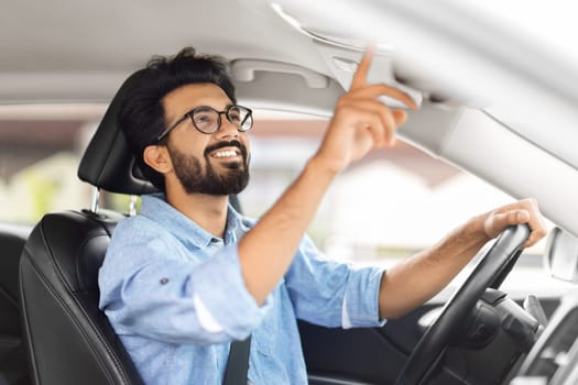 Cheerful indian man driver pushing button on car panel