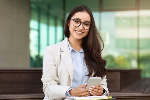 Happy pretty confident young european lady in suit, glasses enjoy work, typing on smartphone
