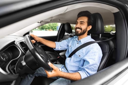 positive young indian man sitting in car on driver seat
