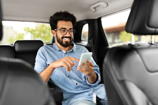 Cheerful indian guy chatting with friends while sitting in taxi