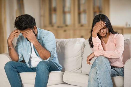 Young Hindu spouses distressed, sitting apart at home on sofa