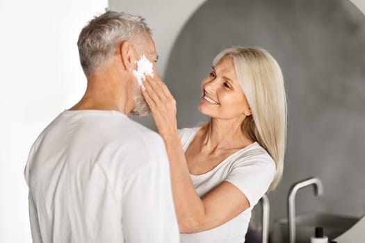 Loving Mature Wife Applying Shaving Foam On Husband's Face In Bathroom