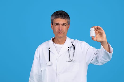Professional medical specialist man stands confidently showing pills jar, studio