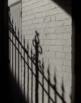 Wrought iron fence casts its stark shadow reflected on the adjacent white brick wall.
