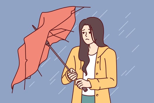 Wet woman stands with broken umbrella in heavy rain, and is sad because of cold and strong wind