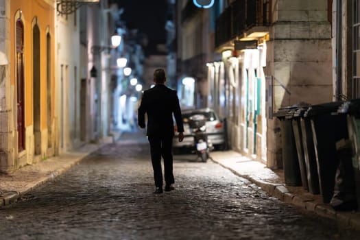 A man walking alone on a historic street at night - view from behind