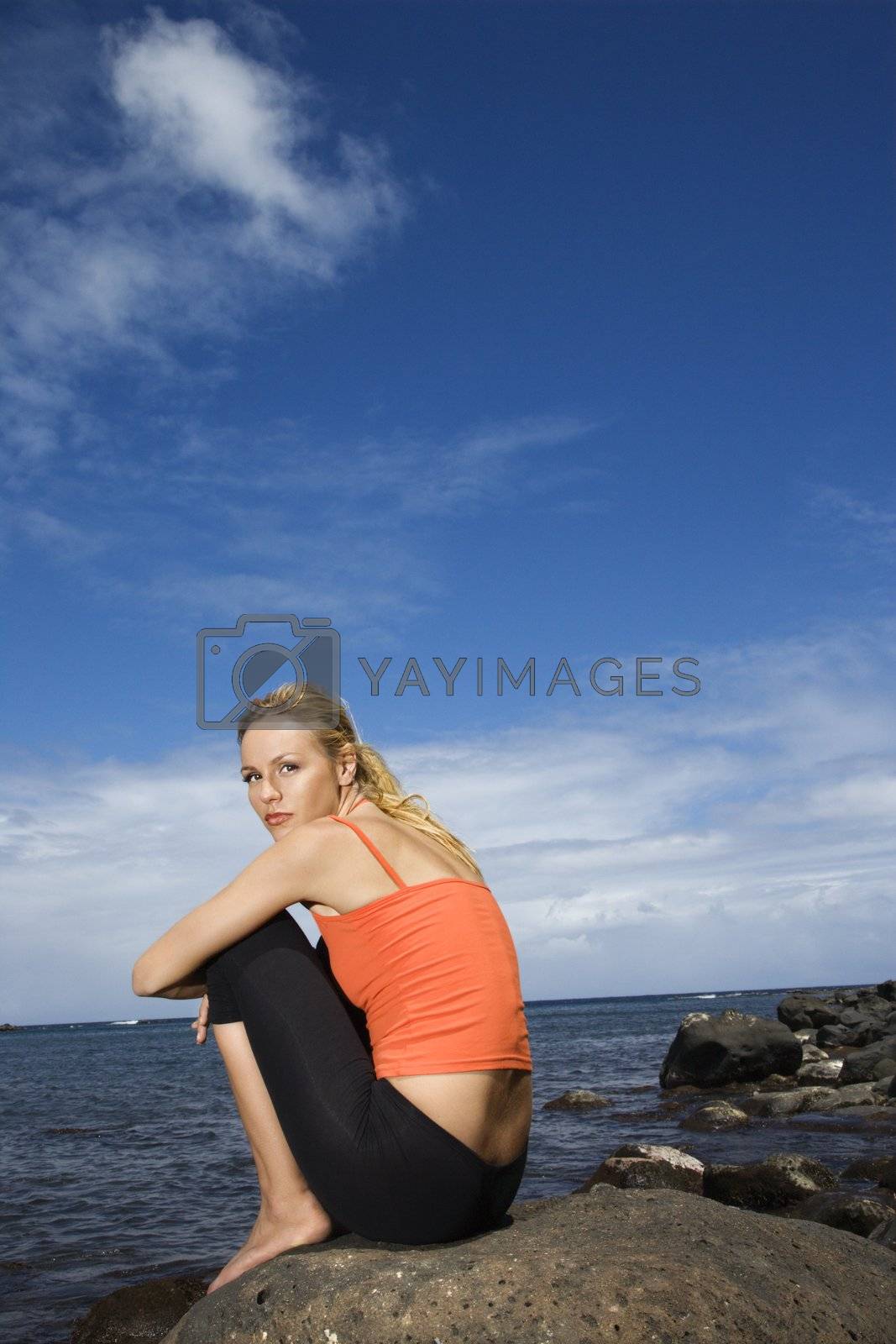 Royalty free image of Woman sitting on rocky shore. by iofoto