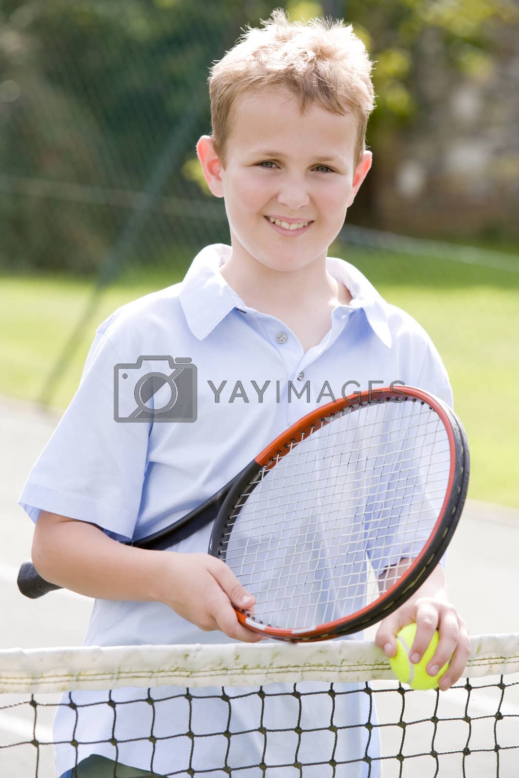 Royalty free image of Young boy with racket on tennis court smiling by MonkeyBusiness