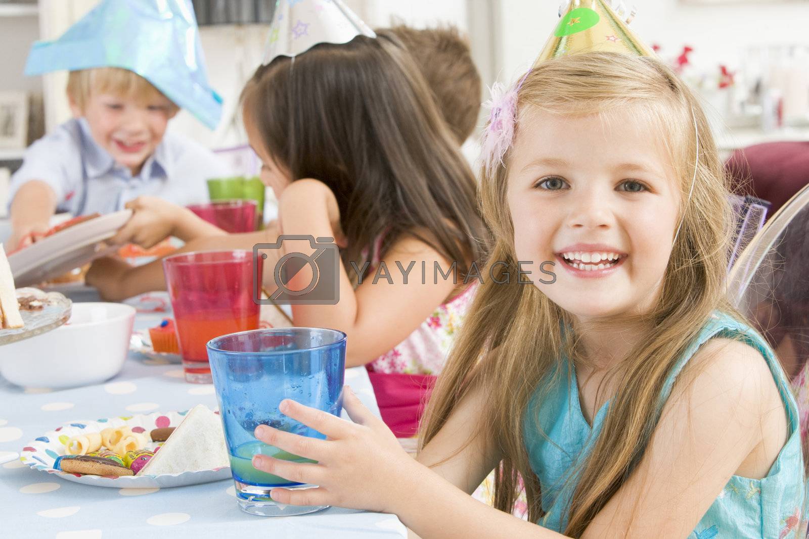 Royalty free image of Young girl at party sitting at table with food smiling by MonkeyBusiness