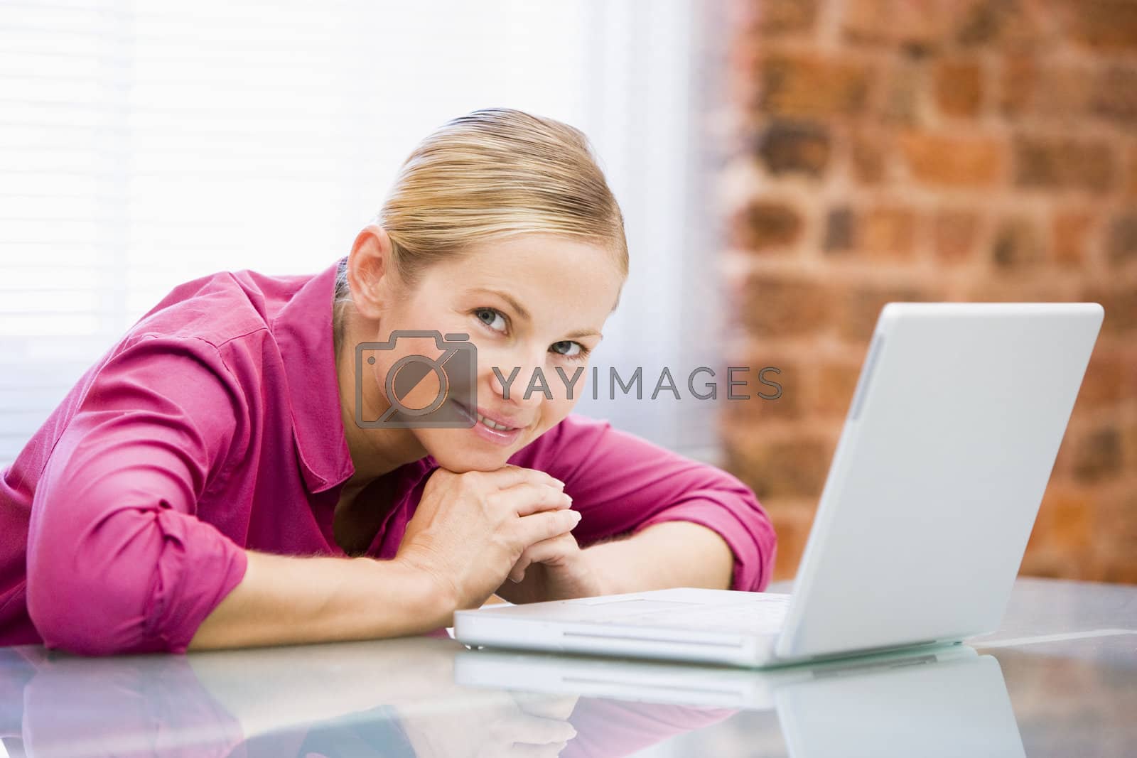 Royalty free image of Businesswoman sitting in office with laptop smiling by MonkeyBusiness
