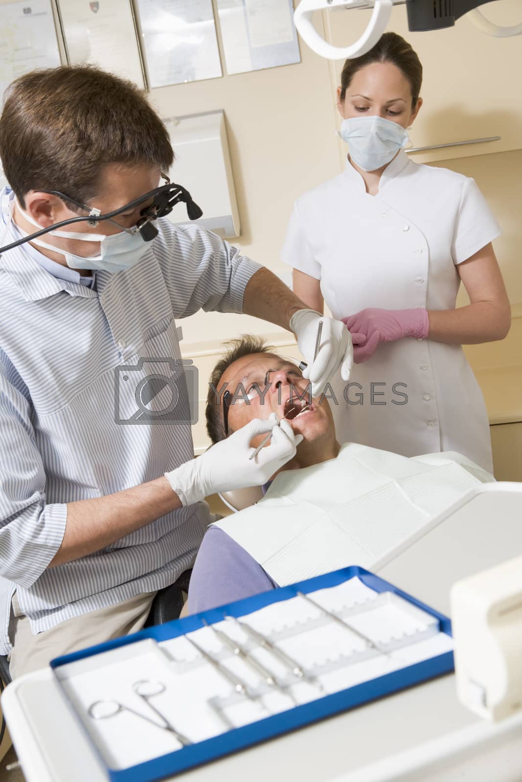 Royalty free image of Dentist and assistant in exam room with man in chair by MonkeyBusiness