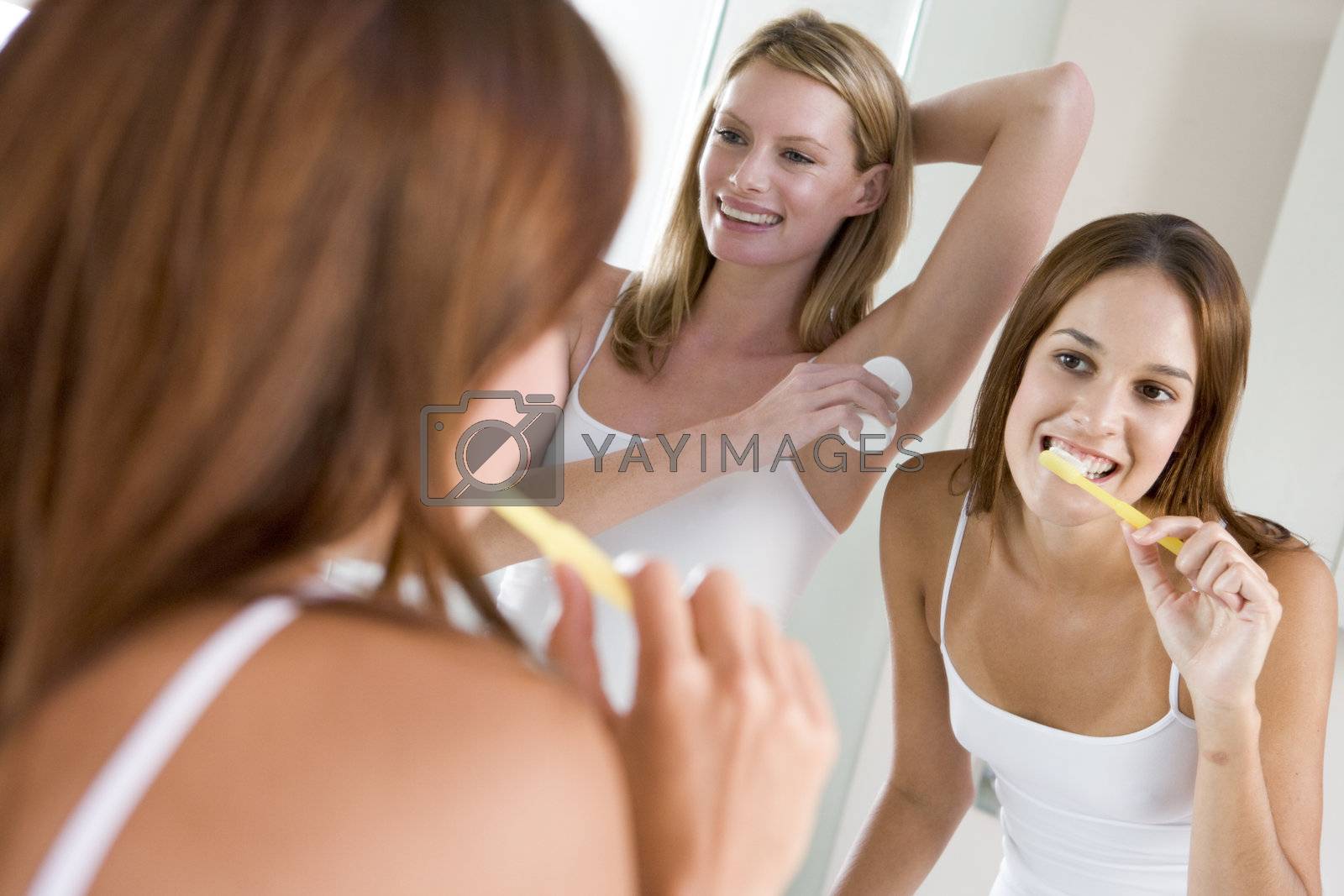 Royalty free image of Two women in bathroom brushing teeth applying deodorant and smil by MonkeyBusiness