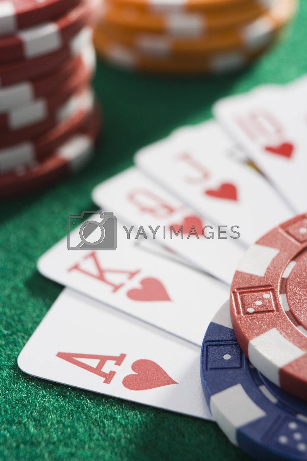 Royalty free image of Playing cards making royal flush in hearts by poker chips by MonkeyBusiness