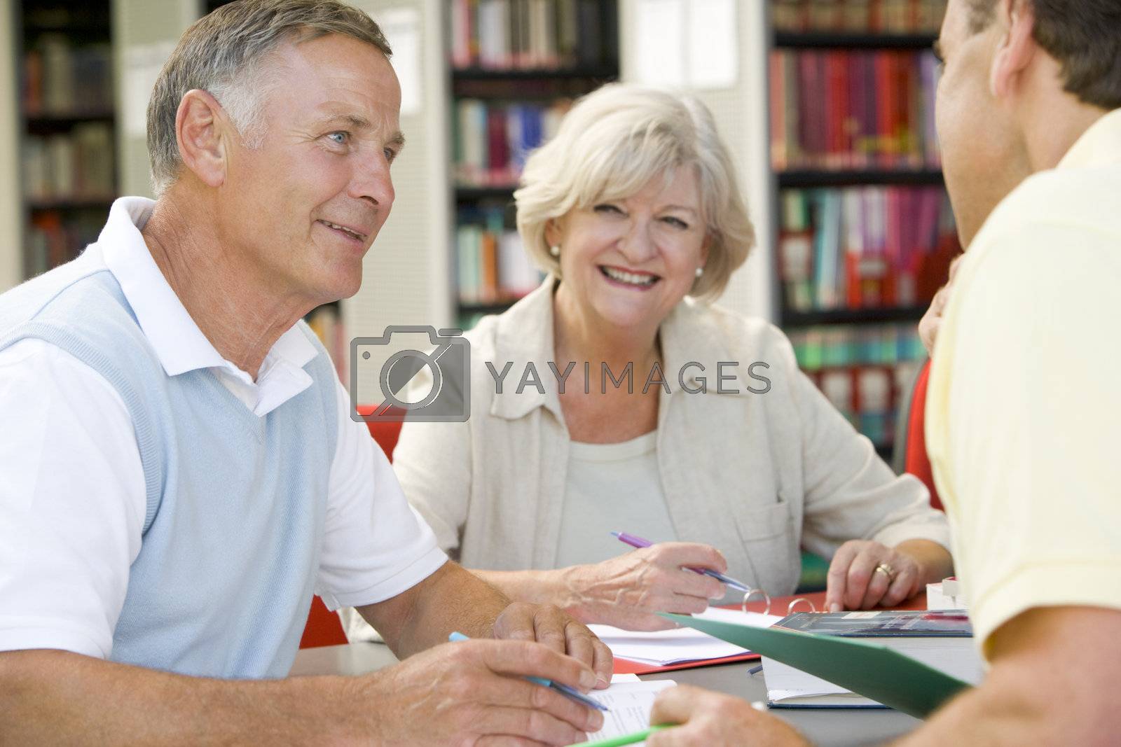 Royalty free image of Three people in library writing in notebooks (selective focus) by MonkeyBusiness