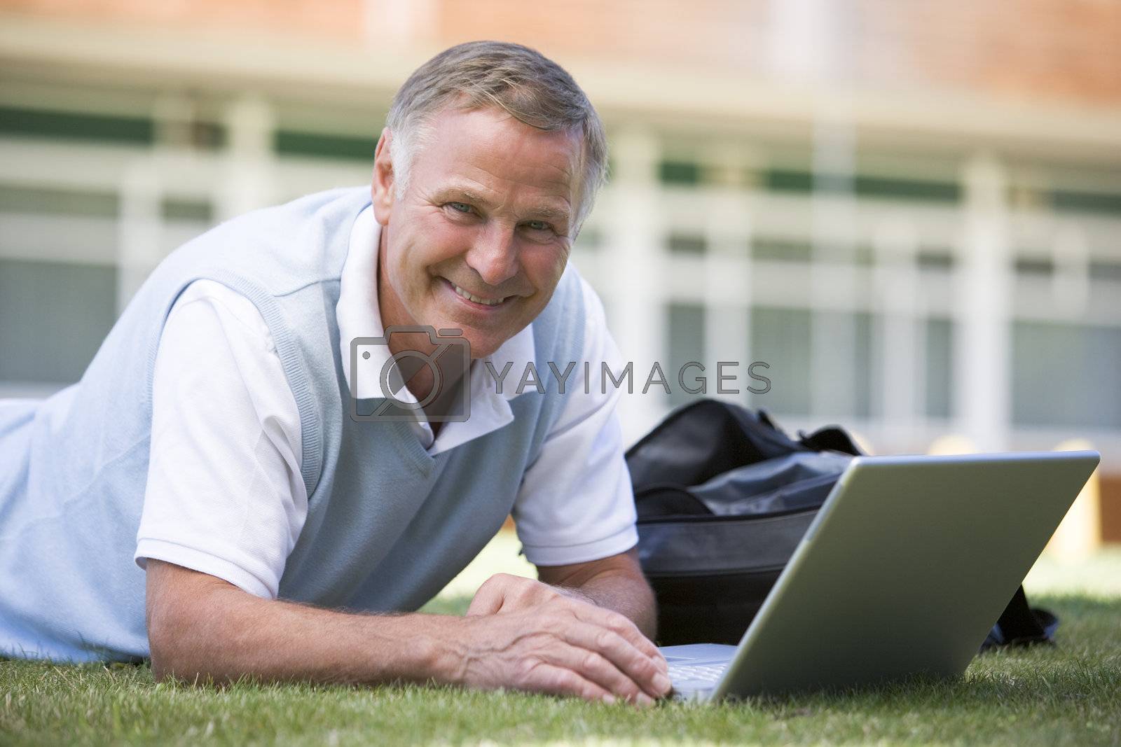 Royalty free image of Man lying on lawn of school with laptop by MonkeyBusiness