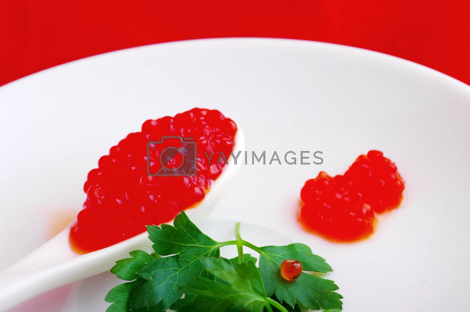 Royalty free image of Spoon with red caviar and greens parsley on a white plate  by dolnikow