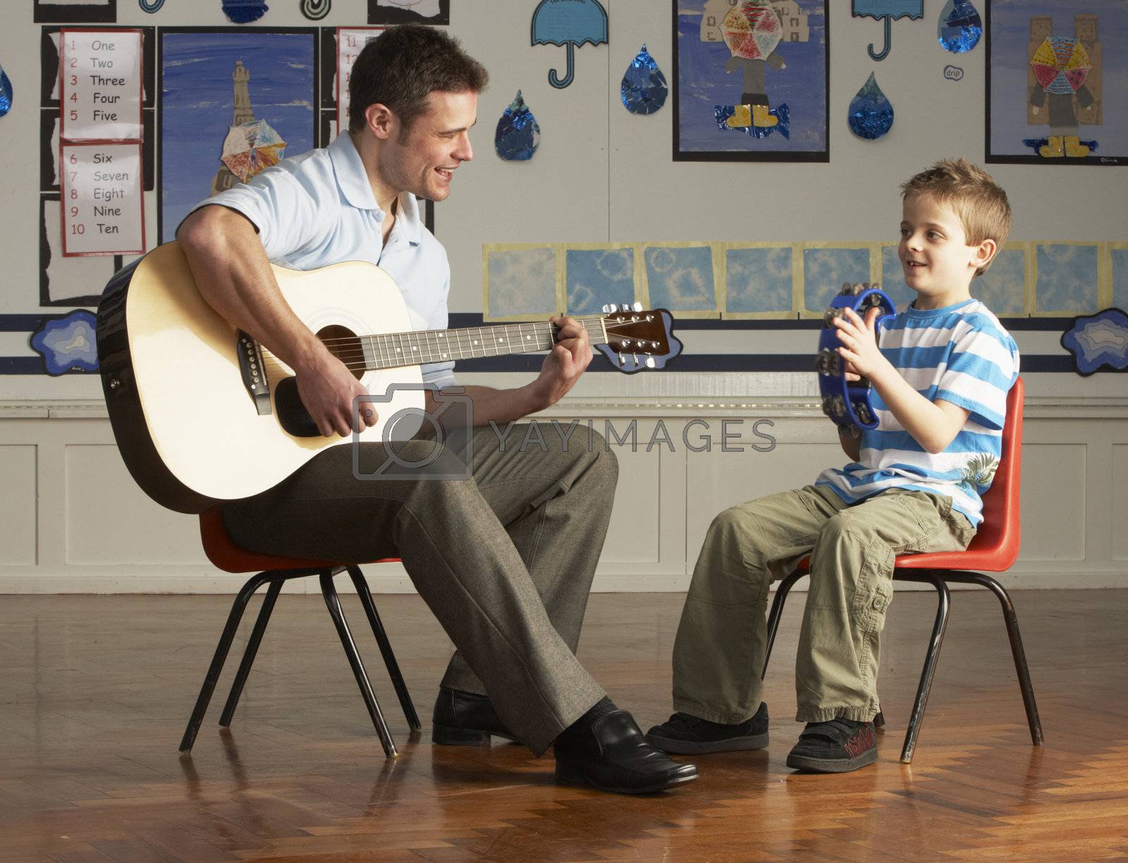 Royalty free image of Male Teacher Playing Guitar With Pupil In Classroom by omg_images