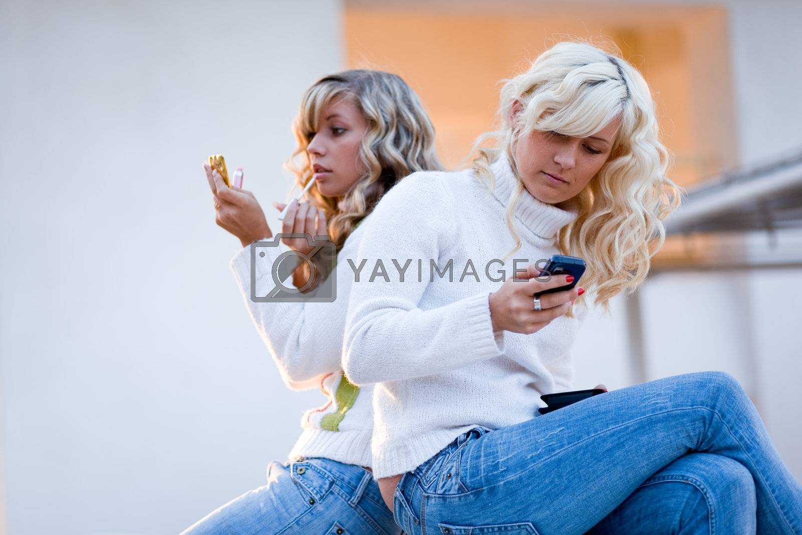 Two teenage girls sit and talking watching mobile phone.