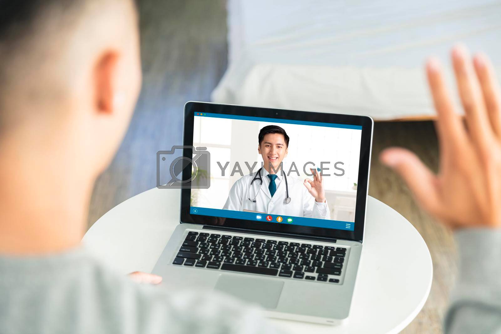 Royalty free image of Back view of man talking to dotor by video call with laptop.Dotor smiling and showing ok gesture. by tomwang