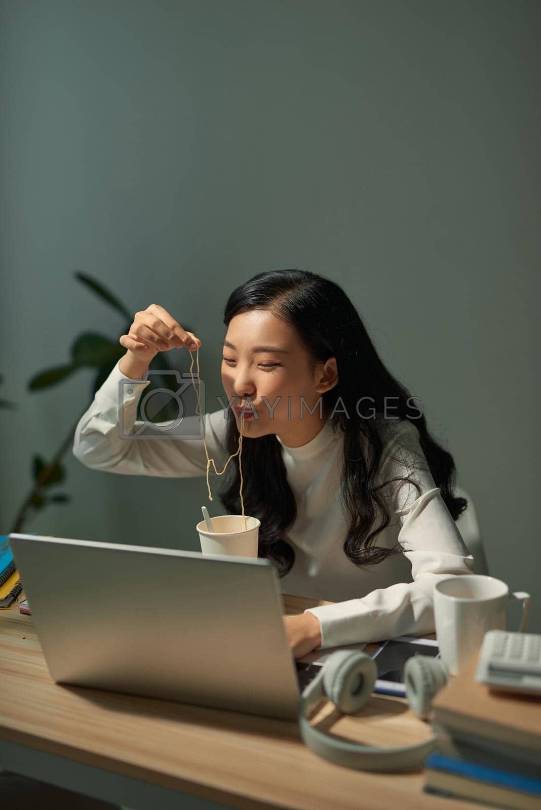 Royalty free image of Hungry student eating noodle while learning at home by makidotvn