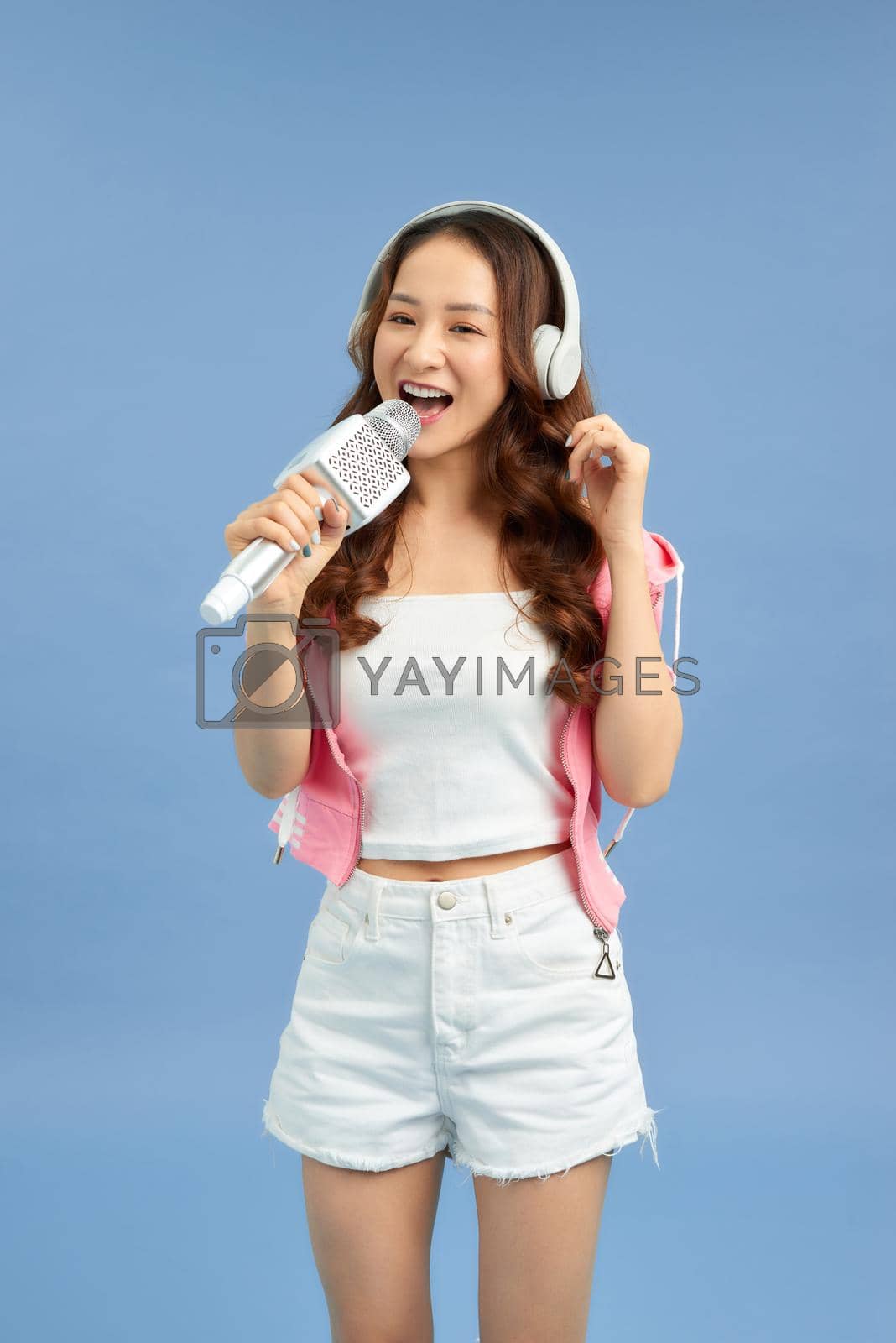Royalty free image of Beautiful Asian woman singing karaoke isolated over blue background. by makidotvn