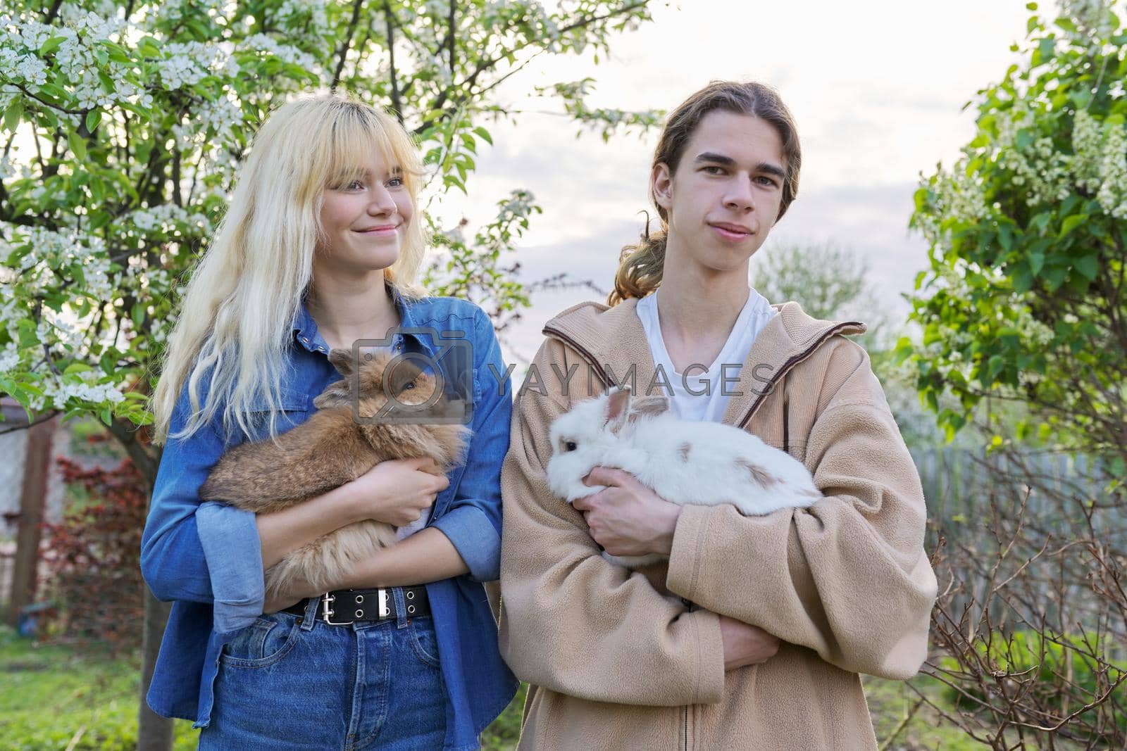 Teenagers with rabbits in their hands, pets a couple of decorative rabbits, nature, spring green blooming garden background