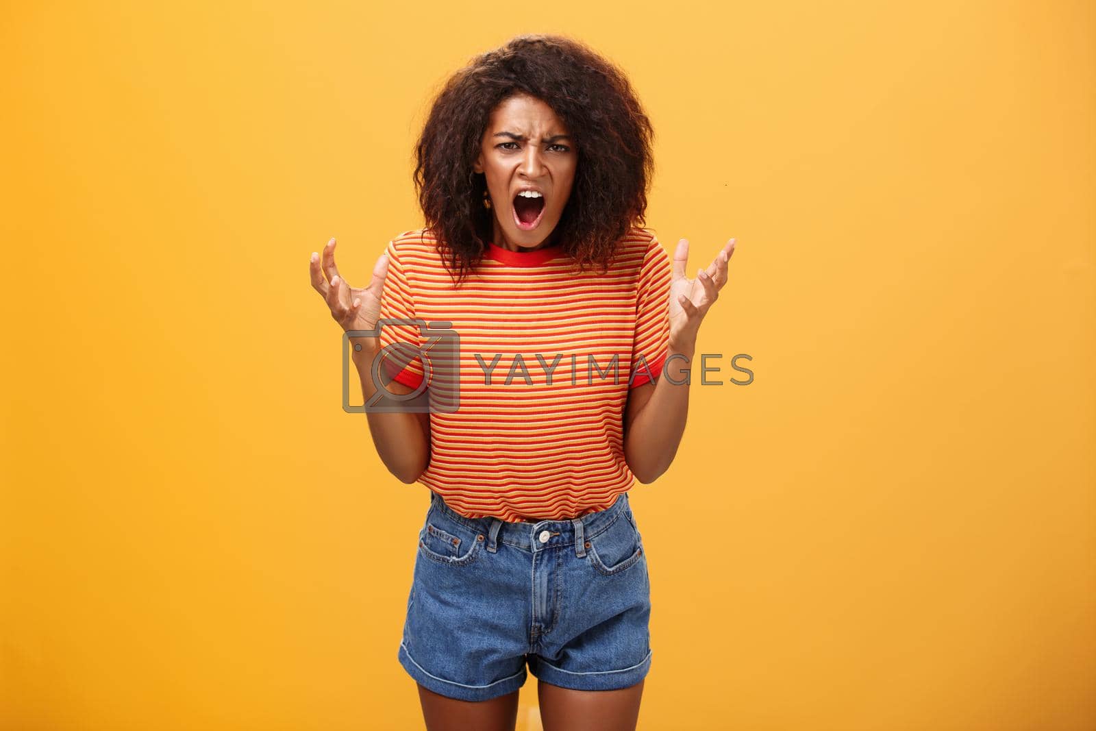 Royalty free image of Pissed and outraged angry african american young female in stylish outfit raising palms gesturing and yelling losing temper arguing with cheating partner feeling fed up over orange background by Benzoix
