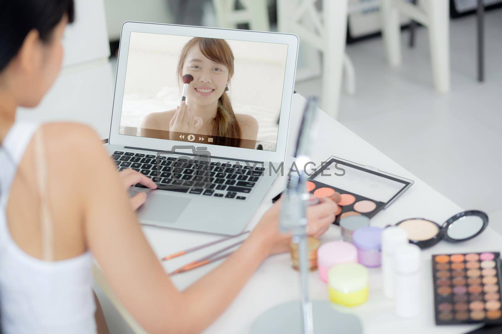 Royalty free image of Beauty of young asian woman with learning makeup with brush on cheek on laptop computer with tutorial course online, female teaching and explain make up with cosmetic on streaming social media. by nnudoo