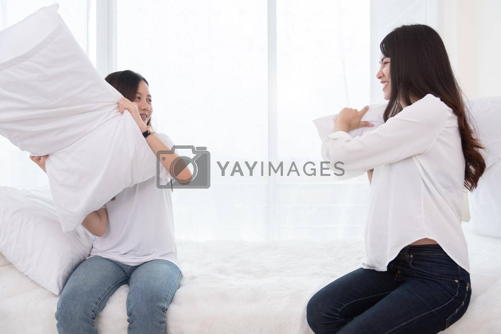 Royalty free image of Two Asian girls doing pillow fight in bedroom as childhood. Lifestyles and People concept. Relation and friendship theme. Couple and friends concept. LGBT and people lifestyle by MiniStocker