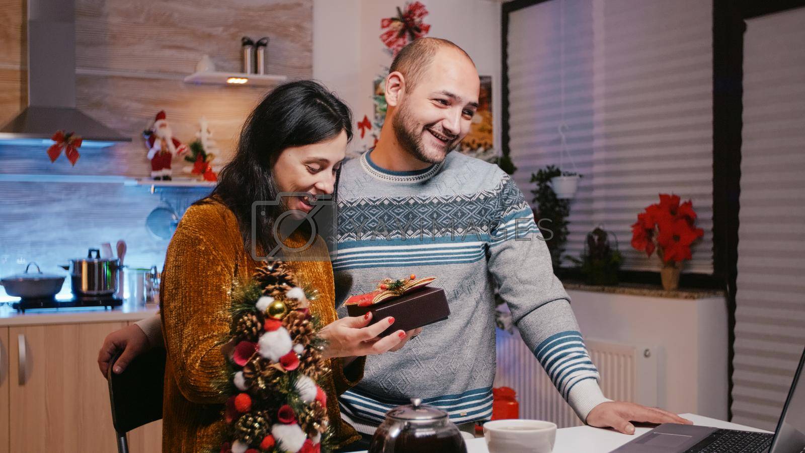 Man and woman receiving gift on video call communication for christmas eve celebration. Festive couple with present box celebrating winter holiday with family on online conference