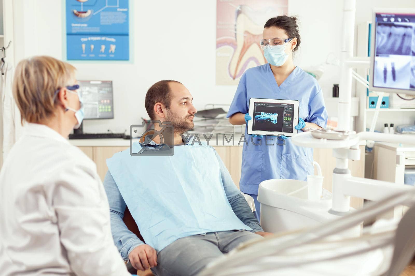 Dentist assistant showing teeth radiography on tablet pc computer screen to sick patient man at dental clinic office. Orthodontist discussing toothache treatment to prevent stomatology problems